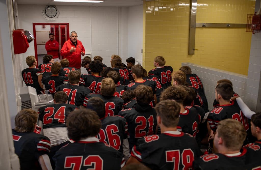 The Baldwinsville Bees varsity football team takes a knee to pray and listen to coaches before taking the field. All coaches emphasized the need to play for the seniors on Senior Night. "Play your nuts off," said one coach.